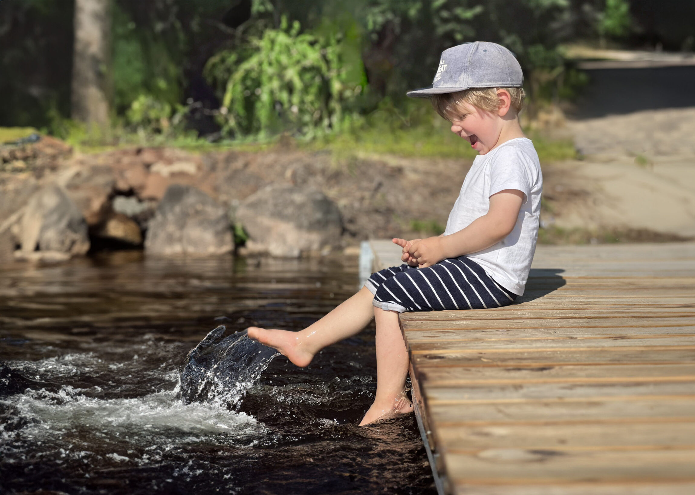 Pieni poika istuu laiturilla jalat vedessä ja nauraa