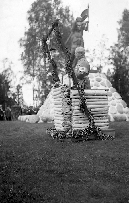 Vuorineuvos Gösta Serlachius seisoo Vilppulan taistelujen muistopatsaan vieressä korokkeella pitämässä puhetta.